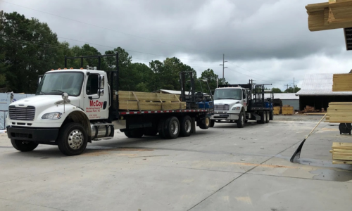 McCoy branded delivery trucks parked at their lumber yard on a cloudy day.